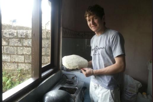 A man from Afghanistan is posing in a kitchen, holding a bread he made